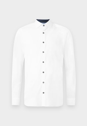 Camicia bianca a maniche lunghe con colletto standard. Presenta bottoni blu navy e un colletto interno a contrasto. Tessuto di cotone morbido.