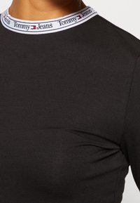 Top negro ajustado de tela elástica con un collar de marca en blanco, azul y rojo que presenta el texto y el logo de "Tommy Jeans".