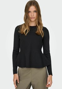 Musta pitkähihainen paita, jossa on pepittiyksityiskohta, valmistettu teksturoidusta kankaasta. Siinä on pyöreä pääntie ja istuvat hihat, yhdistetty khakin värisiin housuihin.