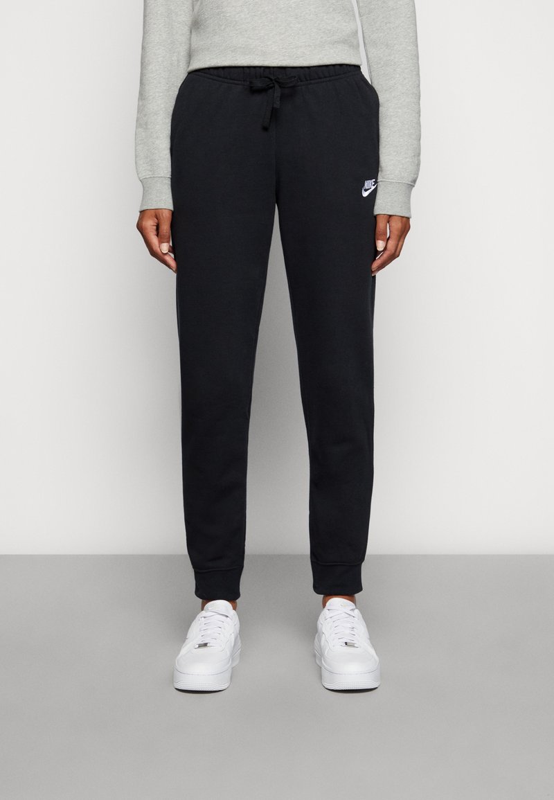 Pantaloni joggers neri in cotone con vita elastica e cordino, con il logo Nike bianco. Abbinati a sneakers bianche.