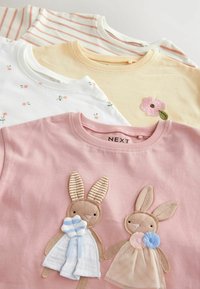 Vier kinder T-shirts: roze met konijnen appliqué, wit met bloemenprint, geel met geborduurde bloem en roze gestreept. Katoenen materiaal.