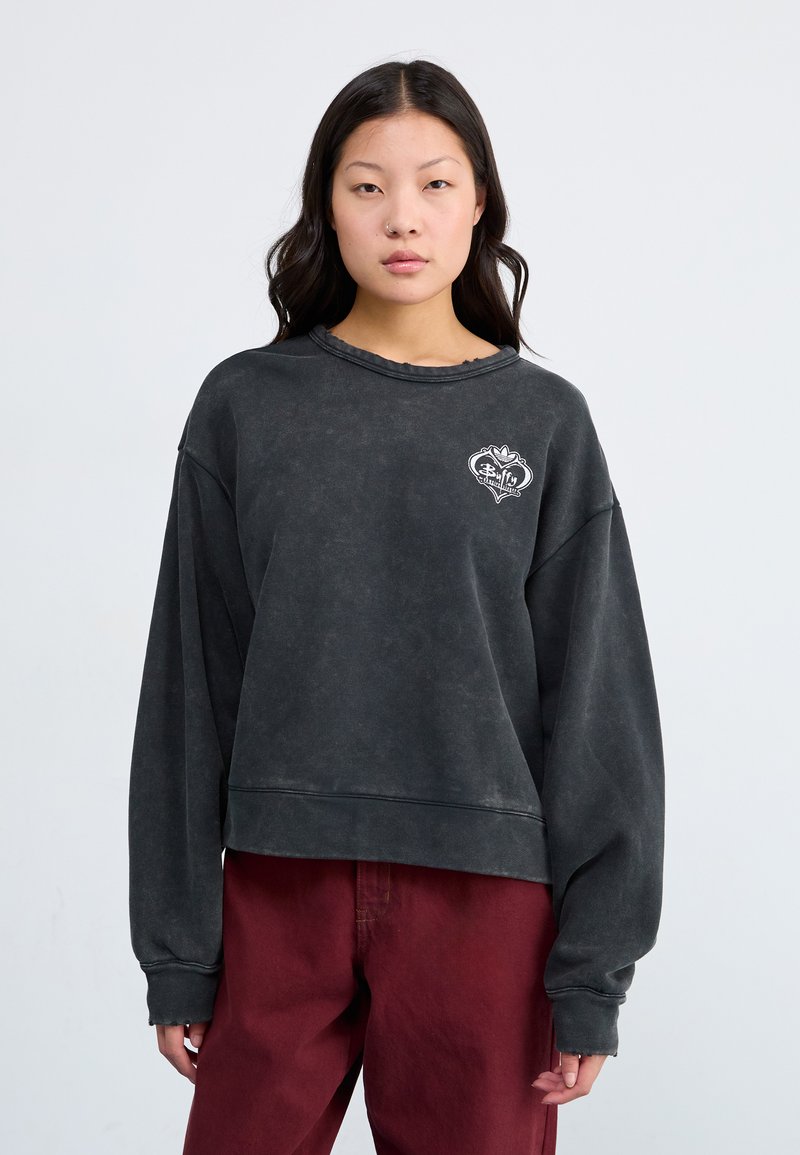 Sudadera nera oversize con un finish sbiadito, maniche lunghe e scollatura rotonda. Presenta un logo a forma di cuore stampato in bianco sul petto.