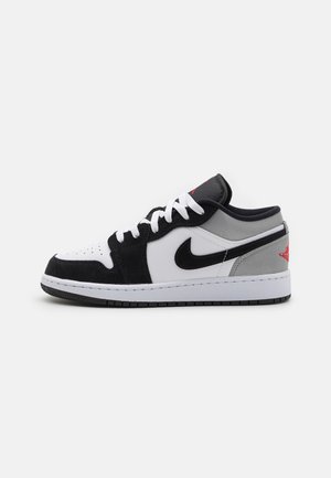 Low-Top Sneaker in Schwarz, Weiß und Grau mit schwarzem Nike Swoosh, weißen Schnürsenkeln und rotem Logo an der Ferse, auf weißem Hintergrund dargestellt.