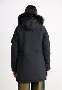 Svart parkasjacka med en foder med päls, med en insydd midja, blixtlås framtill och funktionella sidofickor. Matt textur, medellång design.