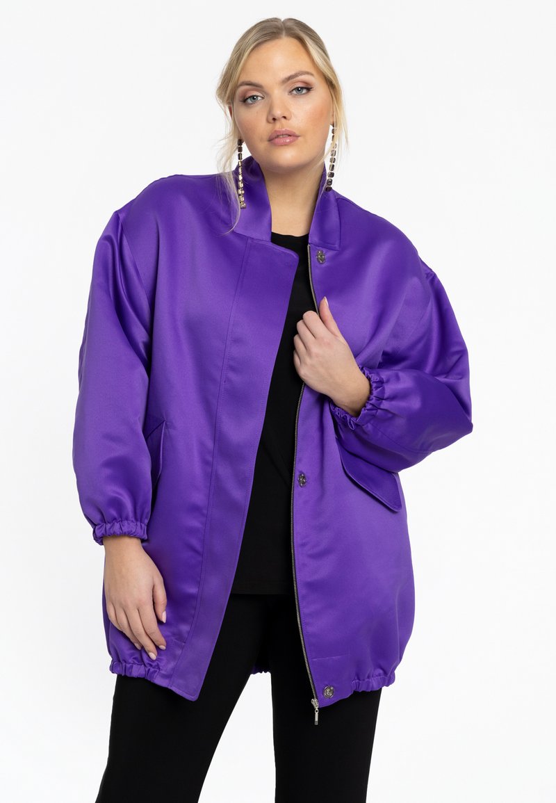 Veste bomber en satin violet avec un col montant, des poignets élastiques et une fermeture éclair à l'avant. Équipée de poches latérales et d'une coupe décontractée.