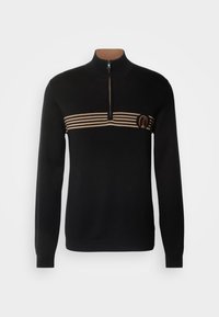 Pull noir à manches longues avec un col marron à fermeture éclair partielle et trois bandes horizontales beige sur la poitrine avec un petit écusson rond.