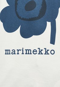 Μπλε αφηρημένο σχέδιο λουλουδιού πάνω από τη λέξη "marimekko" σε λευκό ύφασμα.