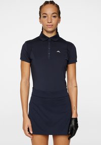 Robe de golf bleu marine avec un col polo, des manches courtes et une silhouette ajustée. Présente un design texturé et un petit logo sur la poitrine.
