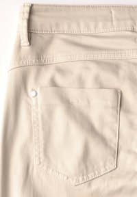 Tissu en denim beige avec une poche arrière rectangulaire dotée de bords cousus et d'un bouton en métal accentuant le haut.