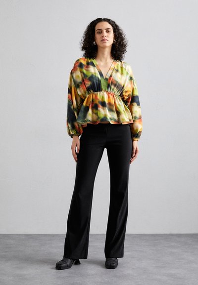 Bluză multicolor cu decolteu în V și talie elastică, având mâneci lungi și un model abstract. Asortată cu pantaloni negri evazați și pantofi.