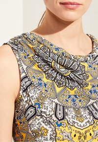 Ærmeløs top med draperet halsudskæring, indviklet mønster i sort, gul og blå, med en glat tekstur og elegante designdetaljer.