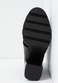 Botín negro con tacón, que presenta una suela de goma texturizada, un tacón cuadrado y un upper liso con sutiles detalles de costura.