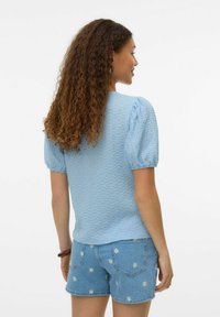 Top azzurro chiaro con texture e maniche corte a sbuffo, abbinato a pantaloni corti in denim chiaro con ricami bianchi a fiori sul tessuto.