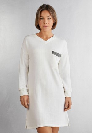 Vitt, ribbat kläddress med långa ärmar och V-ringning. Har en fickdetalj i svart och silver. Sidslitsar vid fållen. Slät textur.