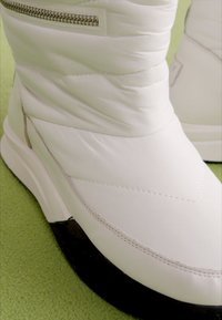 Białe ocieplane zimowe buty o eleganckim designie, z czarną gumową podeszwą, szarym przeszyciem i szczegółowym zapięciem na zamek z boku.