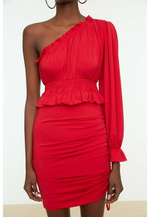 Frau trägt ein rotes Ein-Schulter-Kleid mit Rüschendetails an der Taille und einem langen, aufgebauschten Ärmel auf einer Seite.