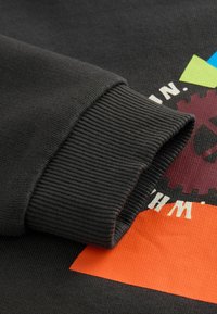 Schwarzer Sweatshirt mit geripptem Bündchen, das ein farbenfrohes Grafikdesign mit geometrischen Formen und Text zeigt.