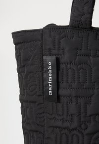 Juodas pagalvėlės tipo rankinė su siuvinėtais tekstų raštais, juoda audinio etiketė su "marimekko" balta spalva ir struktūrizuota viršutinė briauna.