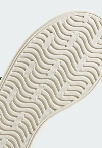 Suela de zapatilla blanca con un patrón de ola texturizado y pequeños acentos elevados para mayor tracción, fabricada con un material de goma duradera.