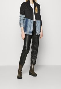 Džínová a černá látková bunda se stříbrnými cvočky, kombinovaná s černými koženými kalhotami a hnědými kotníkovými botami na gumové podrážce.