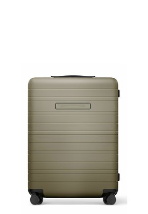 Valise rigide compacte vert olive avec des rainures horizontales, quatre roues noires pivotantes et une poignée supérieure noire.