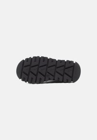 Semelle de chaussure en caoutchouc noir présentant un motif de crampons en zigzag pour une meilleure adhérence, avec un bout arrondi et une surface texturée pour une durabilité accrue.