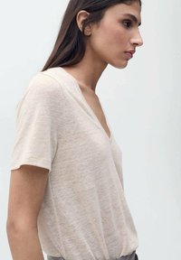 T-shirt beige clair en V fabriqué dans un tissu doux et texturé. Il présente des manches courtes et une coupe décontractée, mettant en valeur le décolleté.