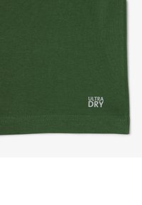 Camiseta verde de tela suave con una textura lisa. Logotipo "ULTRA DRY" impreso en blanco en la esquina inferior derecha.