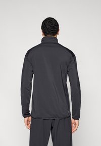 Melna sporta jaka ar augstu apkakli, garām piedurknēm un piegulošu dizainu. Gluda tekstūra ar smalku šuvju detaļu pie pleciem.