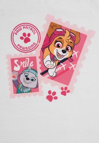 Il tessuto bianco presenta timbri rosa con cani dei cartoni animati, uno con occhiali, e impronte di zampe. Il testo recita "Sorridi" e "PAW PATROL PAWSOME."