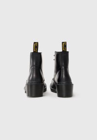 Botine negre din piele cu toc gros, având o talpă texturată și cârlige galbene etichetate "Bouncing". Finisaj neted și cusături decorative.