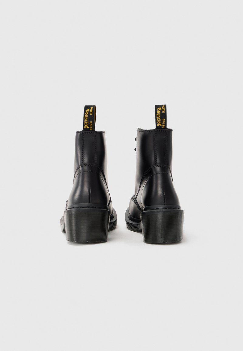 Bottines en cuir noir avec un talon épais, dotées d'une semelle texturée et de tirants jaunes étiquetés "Bouncing". Fini lisse et coutures décoratives.