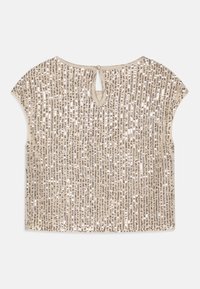 Haut beige à manches courtes orné de sequins argentés verticaux, avec une fermeture par trou de serrure dans le dos et une coupe décontractée.