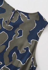 Haut sans manches avec un fond bleu marine, présentant un motif abstrait vert et des contours blancs. Fermeture au dos avec bouton et détail à œillet.