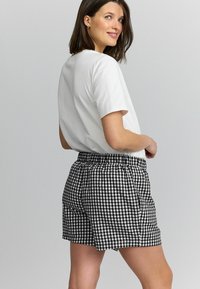 Shorts vichy noir et blanc avec une taille élastique et des poches latérales, associés à un t-shirt blanc simple. Texture de tissu lisse.