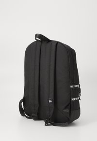 Zaino nero con spallacci imbottiti, forma rettangolare, tessuto testurizzato e un'etichetta visibile con la scritta "NEW YORK" in bianco. Presenta una maniglia superiore.