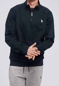 Mörkblå zip-up sweatshirt i bomullsblandning, med ståkrage och en liten vit logotyp på bröstet, samt ribbade ärmslut.