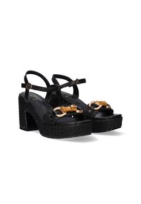 Sandalias de plataforma negras con una suela tejida texturizada. Presentan una cinta ancha con herrajes en tono dorado y correas ajustables en los tobillos.
