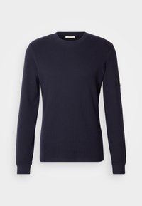 Granatowa, długorękawowa koszulka z okrągłym dekoltem, wykonana z teksturowanej tkaniny, z prążkowanymi mankietami i małą naszywką z logo na lewym rękawie.