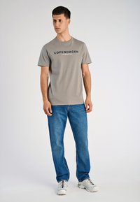 Lichtgrijs t-shirt met korte mouwen met "COPENHAGEN LINDENBERGH" in donkerblauw gedrukt, gecombineerd met blauwe denim jeans en witte sneakers.