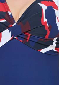 Marine zwemkleding met een diepe halslijn, voorzien van een kleurrijk abstract patroon in rood, wit en blauw; de stof lijkt glad en rekbaar.