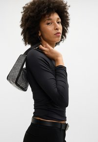 Melnas garām piedurknēm topiņš apvienots ar melnām biksēm, ar spīdīgu akmentiņu rotātu somu, kas viegli nēsāta uz viena pleca.