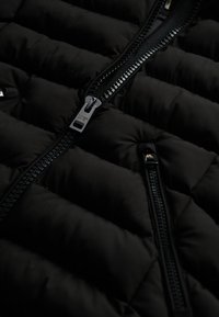 Gilet imbottito nero con design trapuntato, zip lucide e una consistenza morbida. I dettagli con zip e la finitura del tessuto liscia ne aumentano la durata.