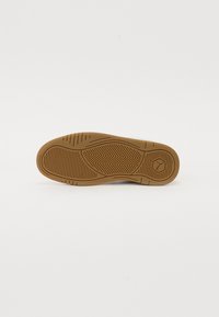 Semelle de chaussure en caoutchouc avec une surface texturée marron, présentant des motifs en chevrons et un logo circulaire.