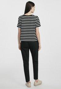 Czarny i biały pasiasty top z krótkim rękawem i okrągłym dekoltem, zestawiony z czarnymi spodniami i jasnymi trampkami. Gładka tekstura materiału.