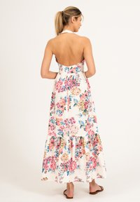 Długa sukienka w kwiatowy wzór, na białym tle, z dekoltem na hals, odkrytymi plecami, falbaną u dołu oraz lekkim materiałem idealnym na ciepłe dni.