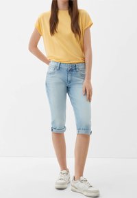 Top amarillo de manga corta, jeans capri azul claro arremangados y zapatillas blancas con suela texturizada, creando un atuendo casual.