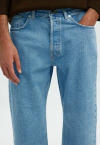 Gaiši zili džinsi ar brīvu piegriezumu. Iespējas klasiskā piecu kabatu dizainā, priekšējā pogu aizdare un viegls izbalējuma efekts.