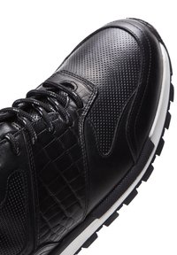 Chaussure de sport noire avec une combinaison de cuir lisse et texturé, des accents perforés, un système de laçage et une semelle en caoutchouc blanche.