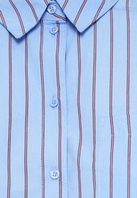 Világoskék gombos ing, függőleges piros csíkokkal, hegyes gallérral és mellzsebbel. Simább szövetből készült, kellemes tapintással.